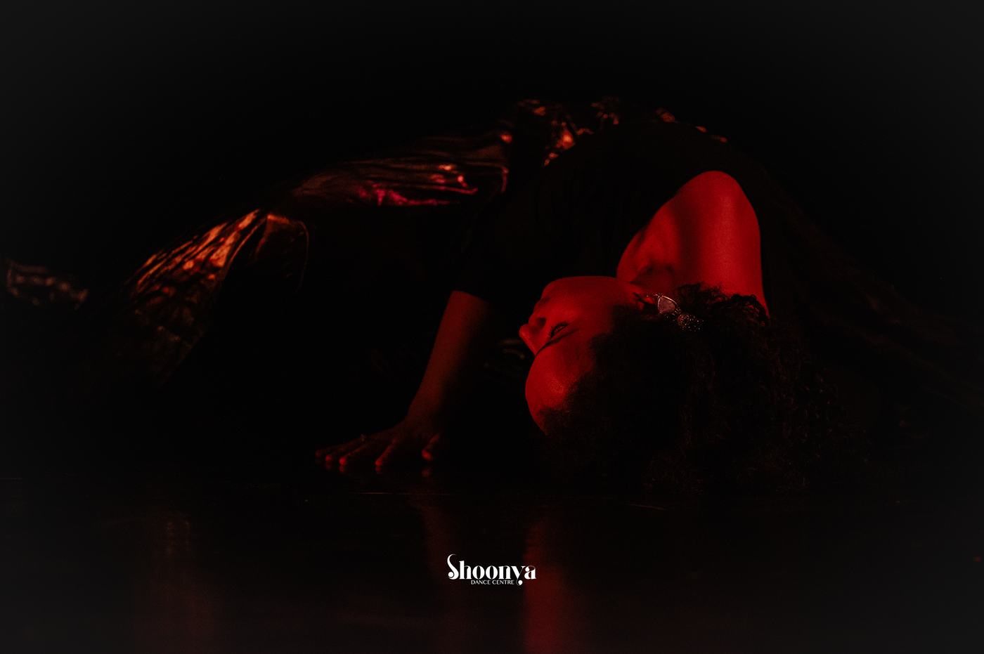 Pranali performing a floor-based dance movement in red stage lighting.