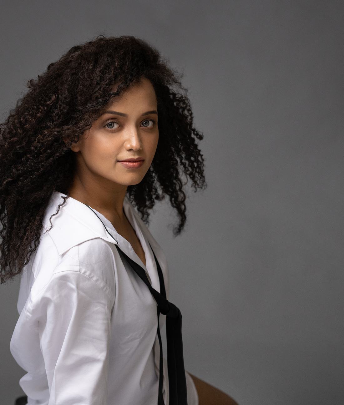 Portrait of Pranali looking into the camera in a white shirt against a grey background.