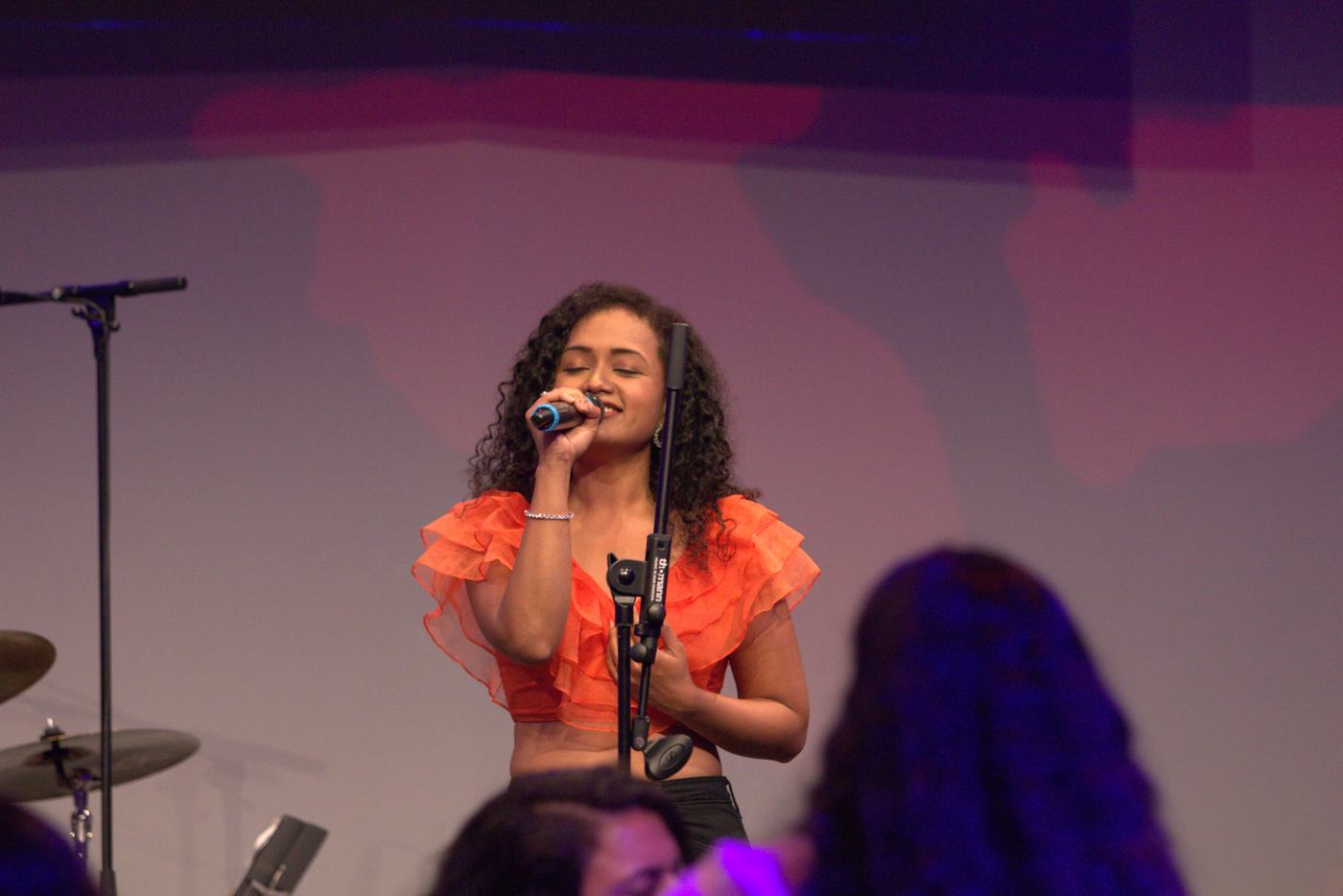 Pranali singing into a microphone on stage in an orange top.